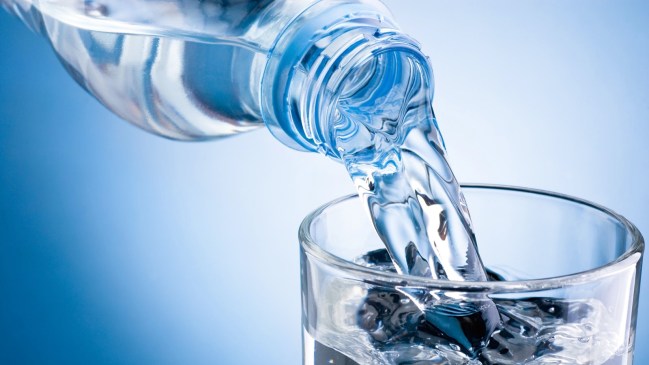 Pouring water from bottle into glass on blue background