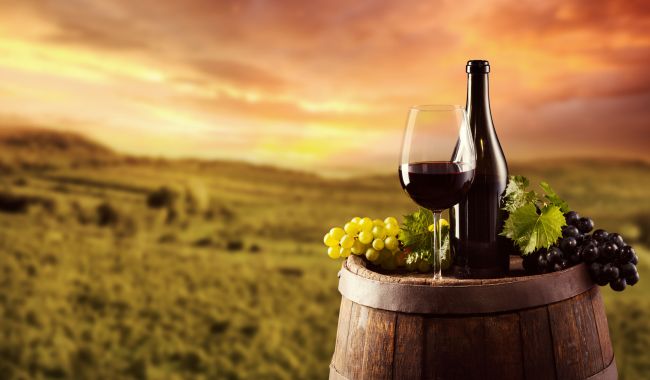46471289 - red wine bottle and glass on wooden keg. vineyard on background